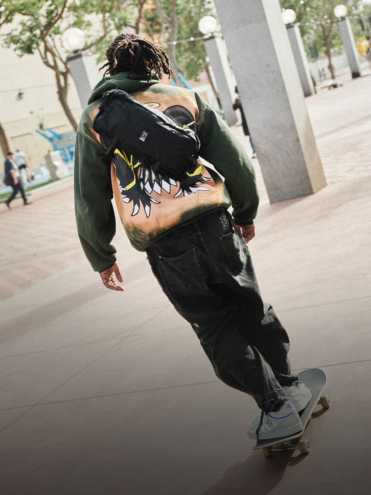 A guy riding a skateboard wearing a Kadet Sling