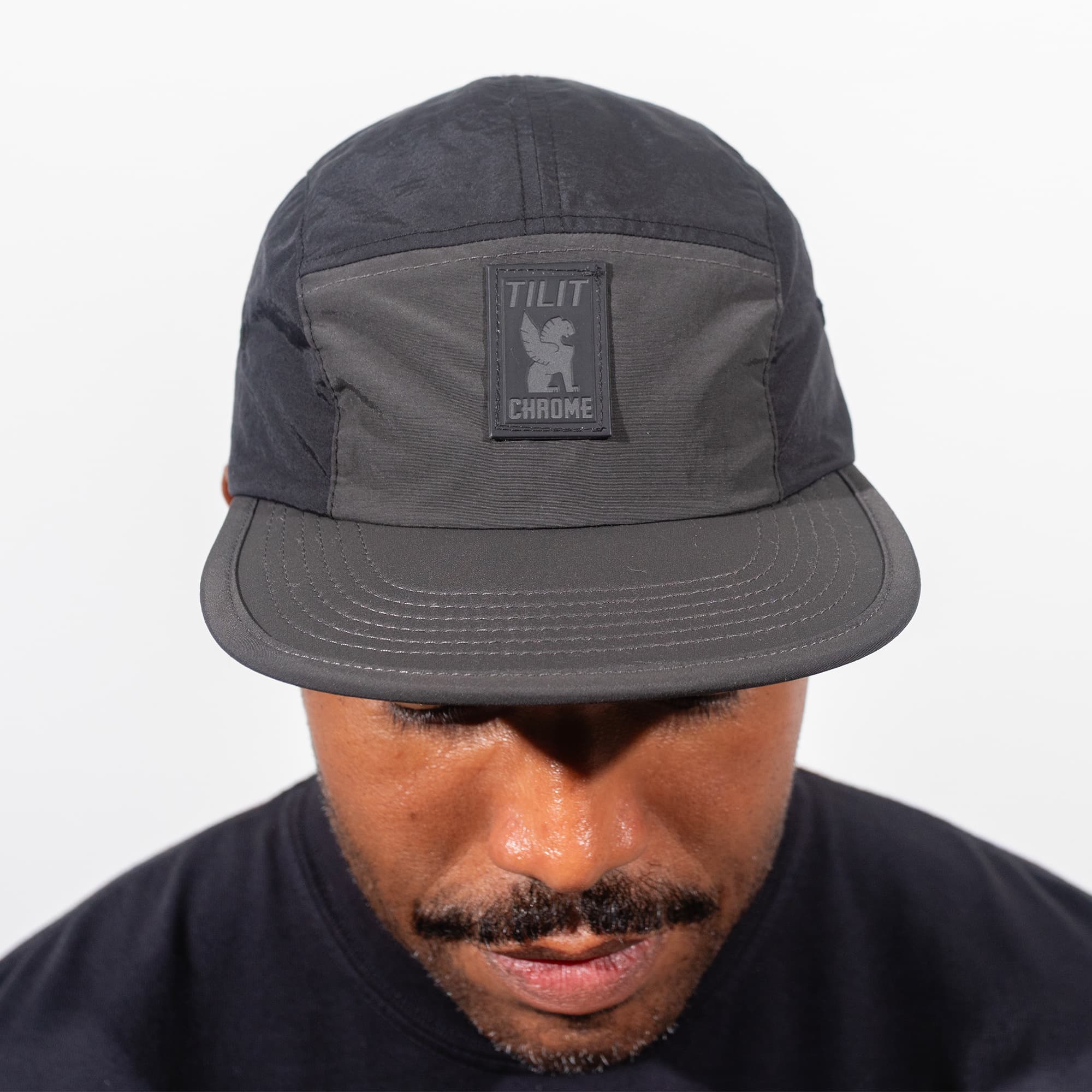 Person wearing the black 5-Panel cap with a visible Chrome x TILIT logo on a white background