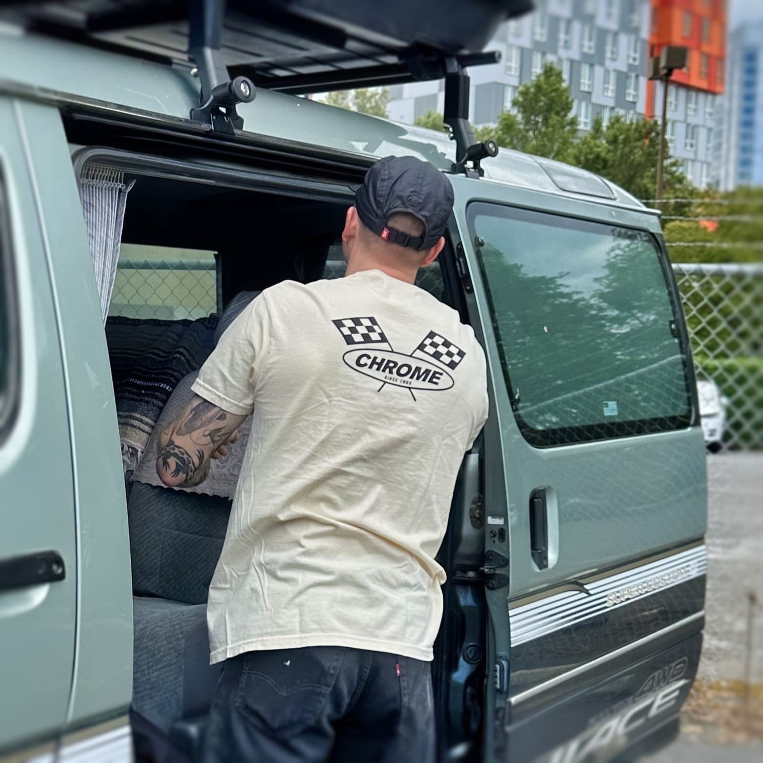 Person getting into a van wearing a 'Chrome' t-shirt with a cityscape in the background.