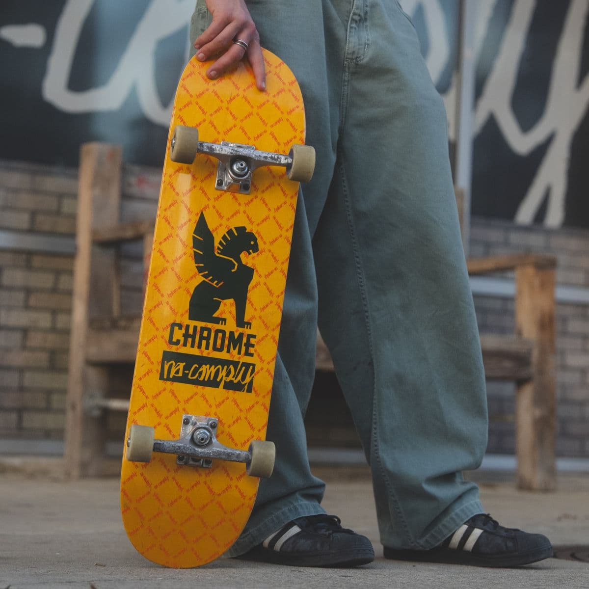 Person holding an orange Chrome x No-Comply skateboard.