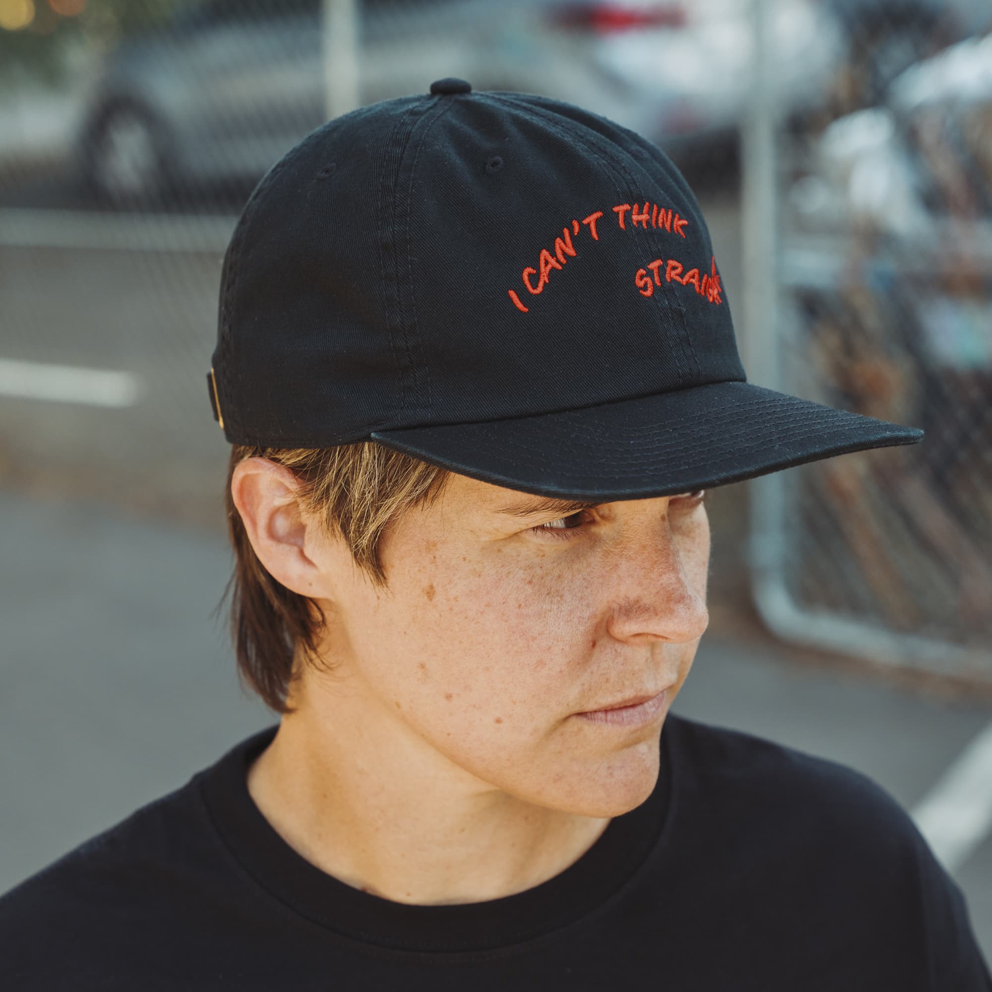 Person wearing a black cap with red text in an urban setting