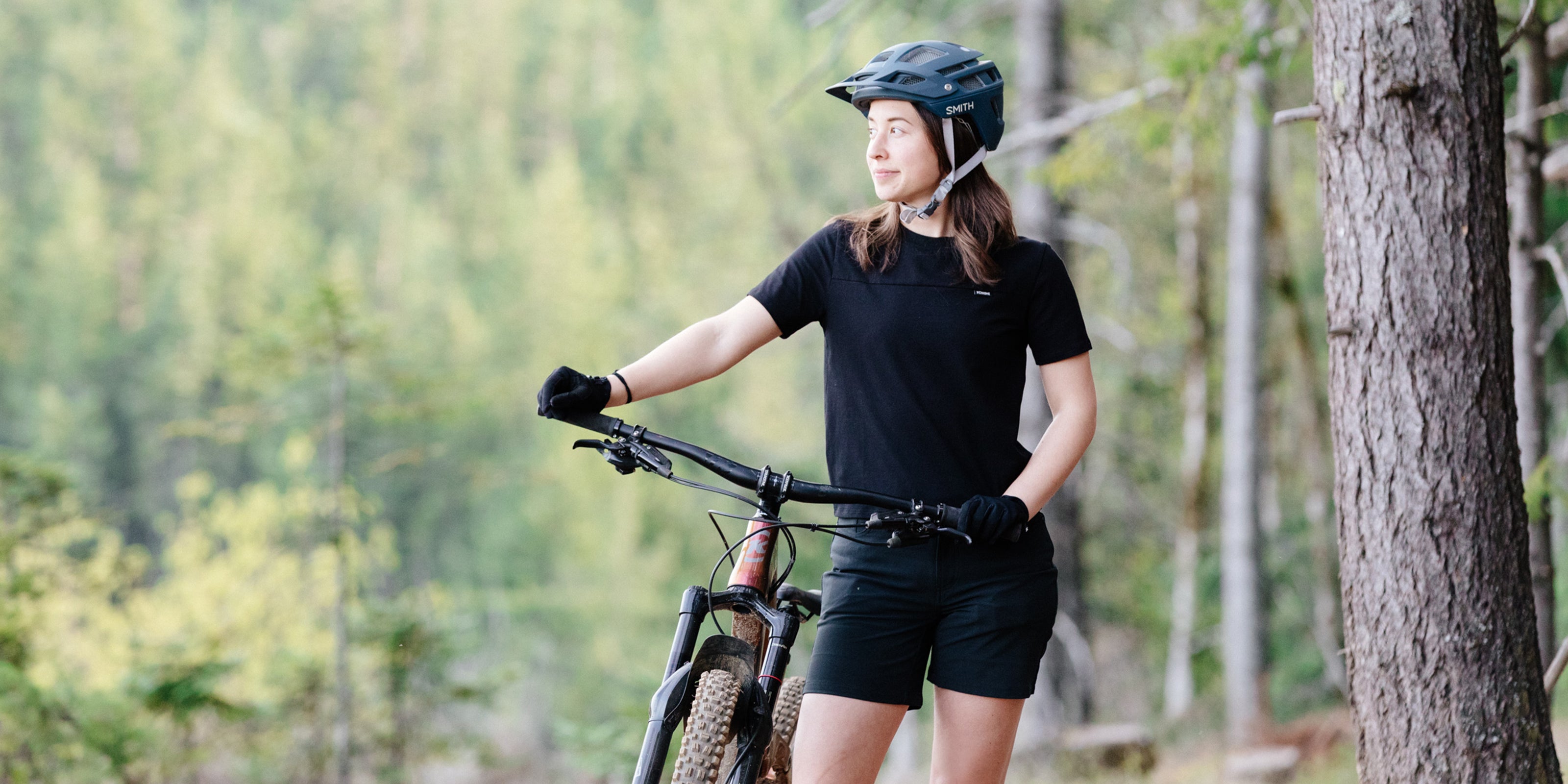 Women's Holman Tee in black worn by a woman riding a mountain bike desktop size image
