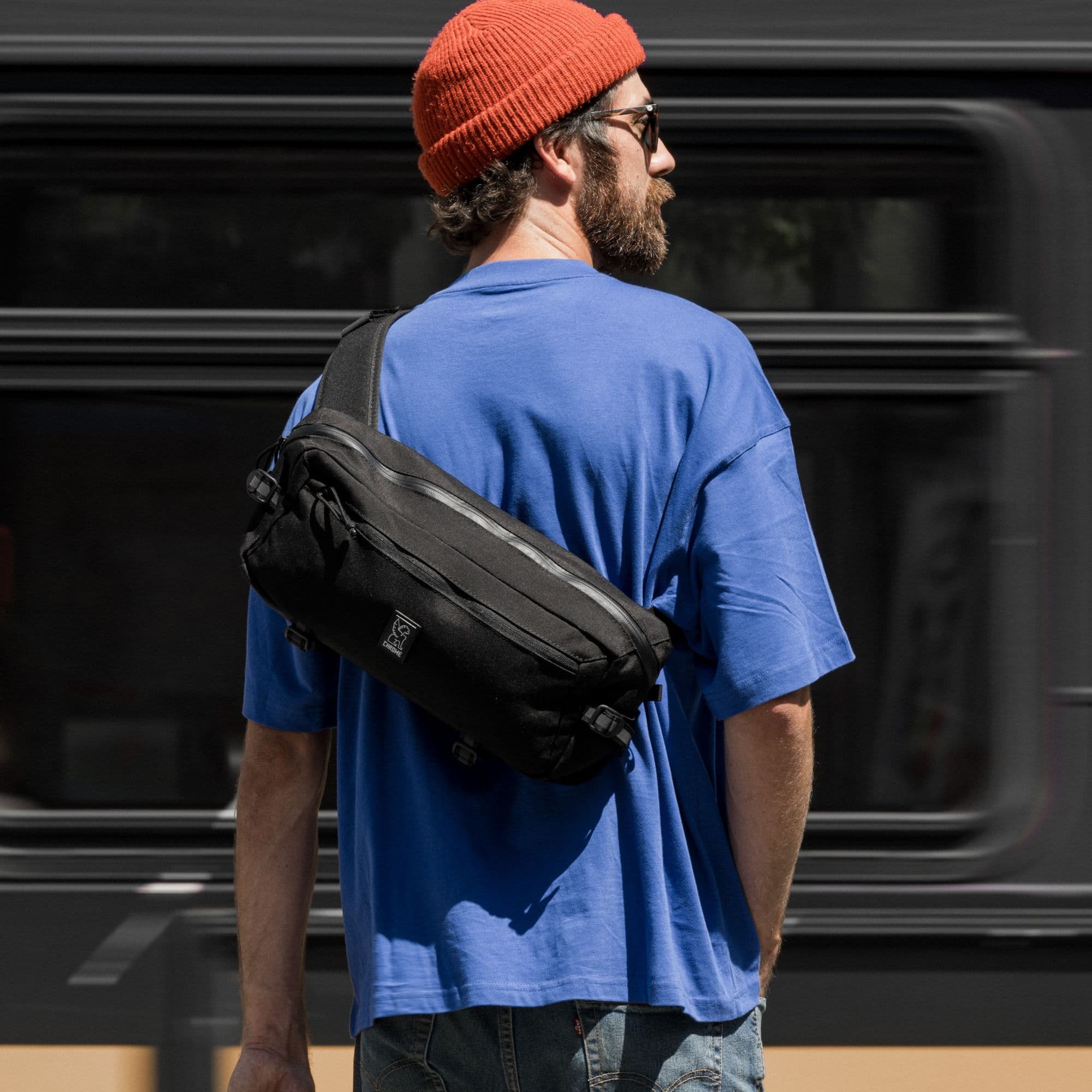 The Kadet 9L Sling in black on a guy waiting for a commuter train