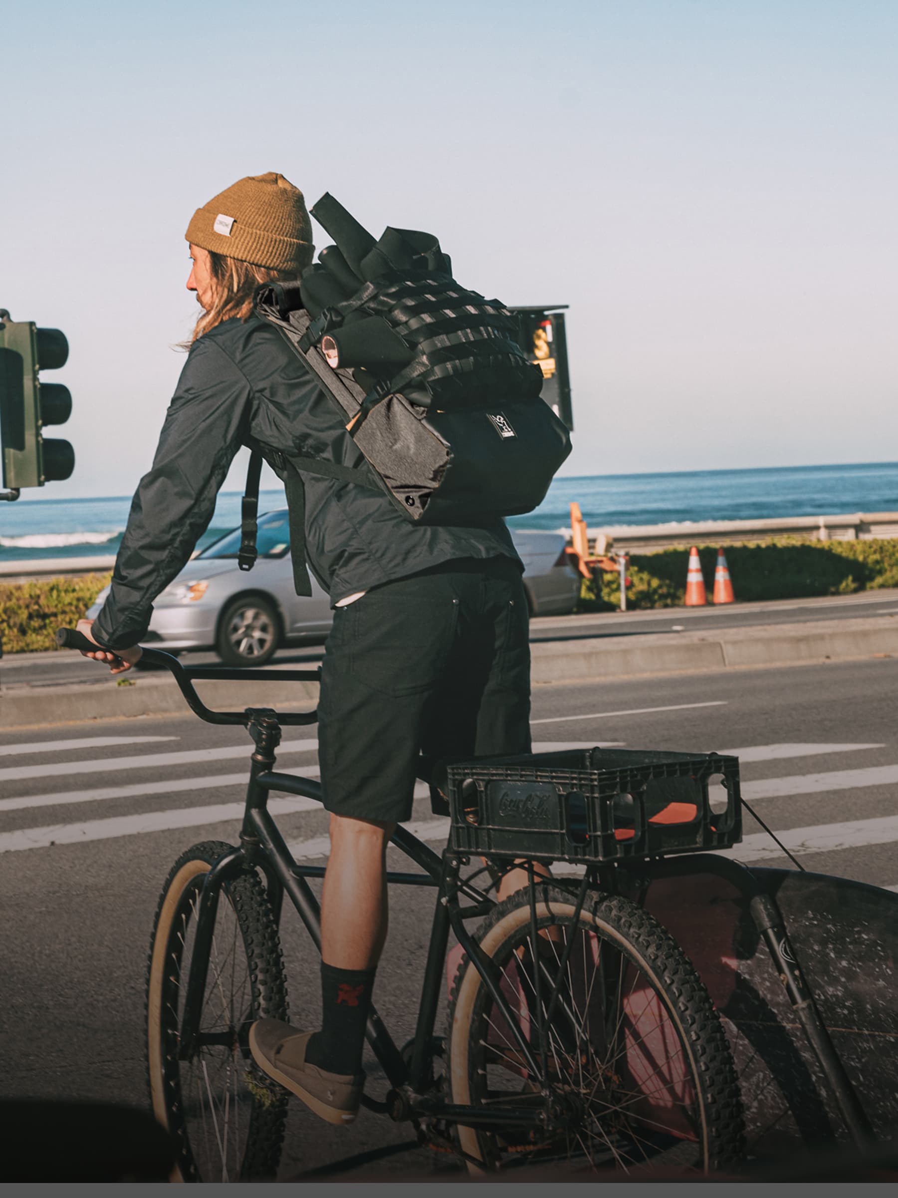 Person with a Barrage backpack riding a bicycle on a road by the ocean.