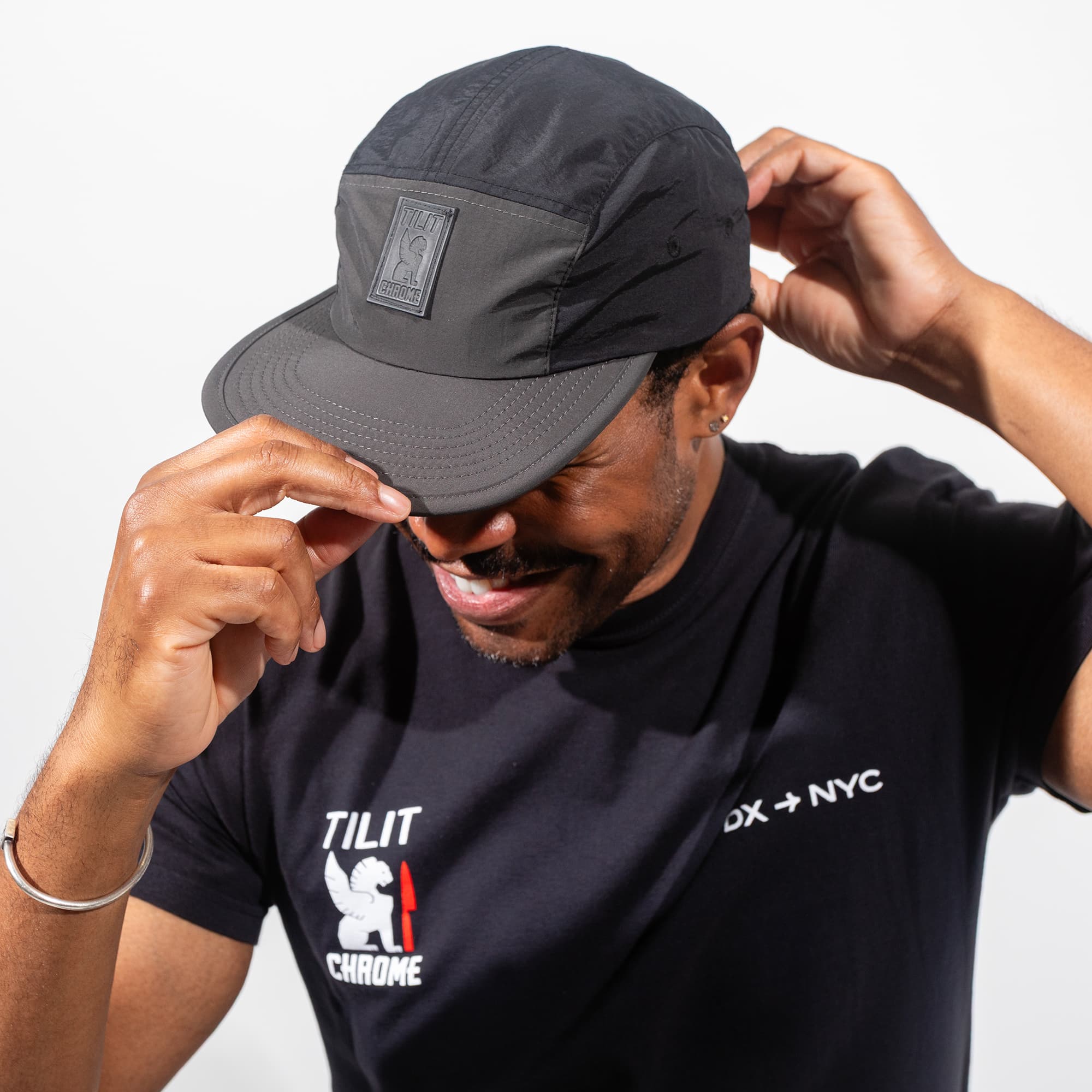 Man wearing the commuter cap and black t-shirt with visible Chrome x TILIT branding on a light gray background