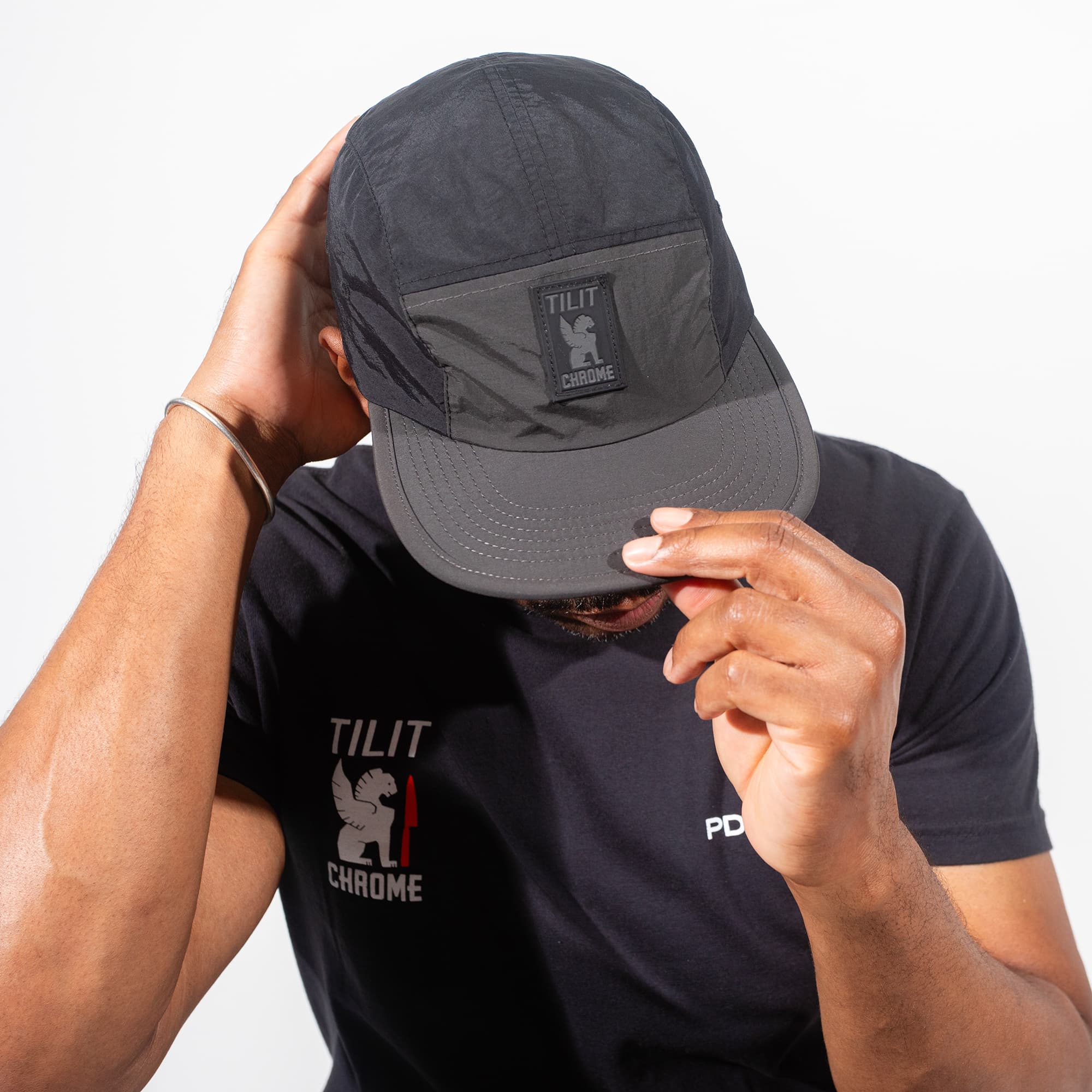 Person wearing a black cap and t-shirt with 'TILIT Chrome' logo on a white background