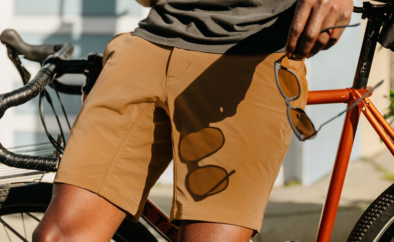 Man wearing the Folsom Short in brown leaning on a bike