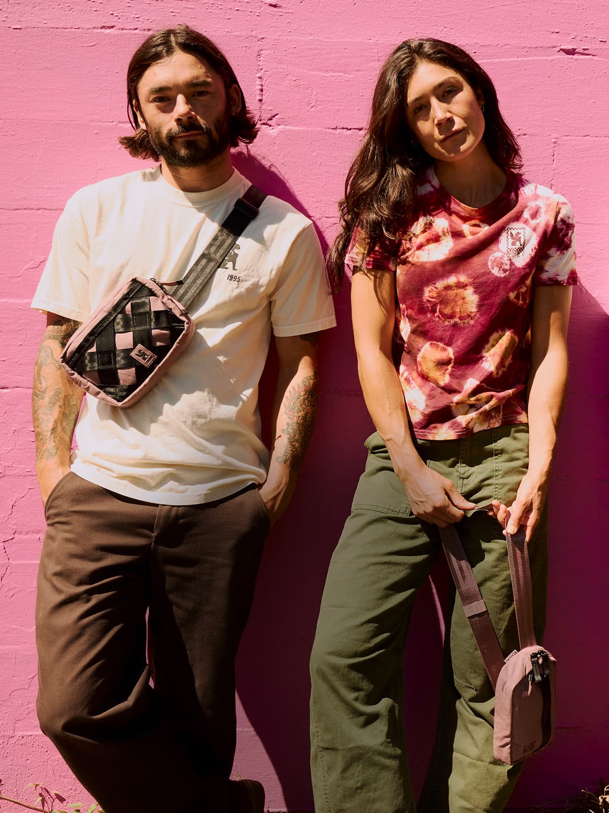 Two people standing by a pink wall with Chrome Sling Bags