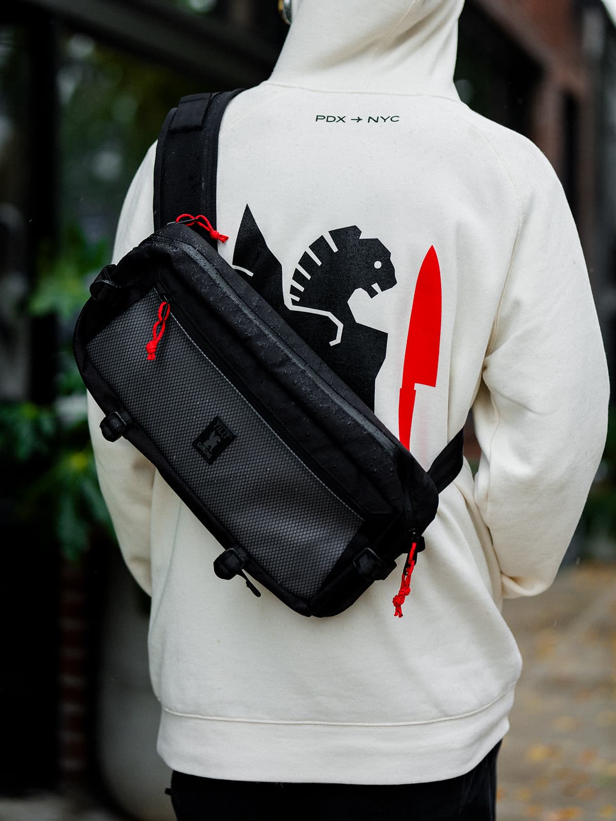 Person wearing a white hoodie with a graphic design and carrying a black crossbody bag.