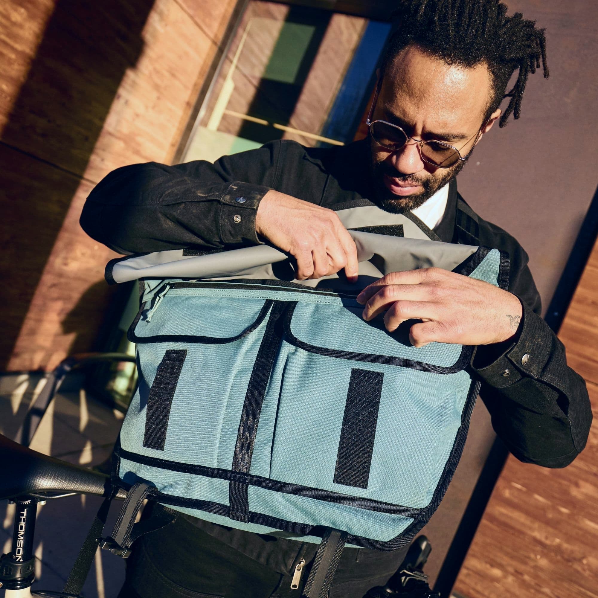 A guy opening the Citizen 24L Messenger in blue #color_steel blue