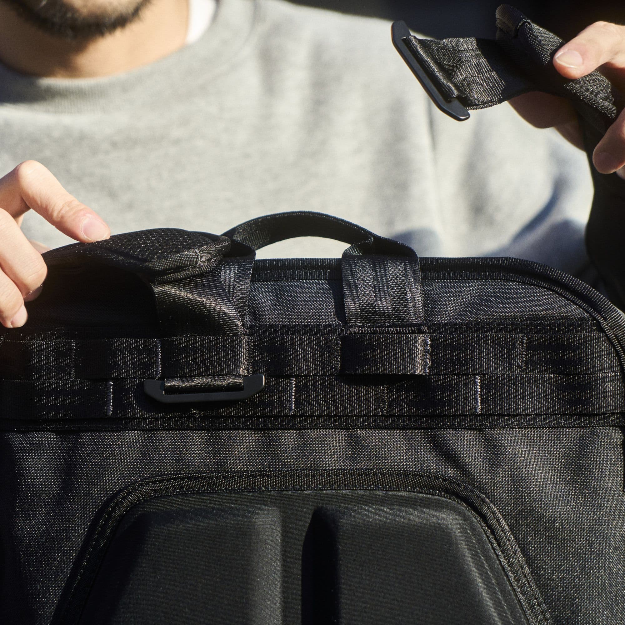 A man showing the backpack strap of the Cohesive unattached from the bag