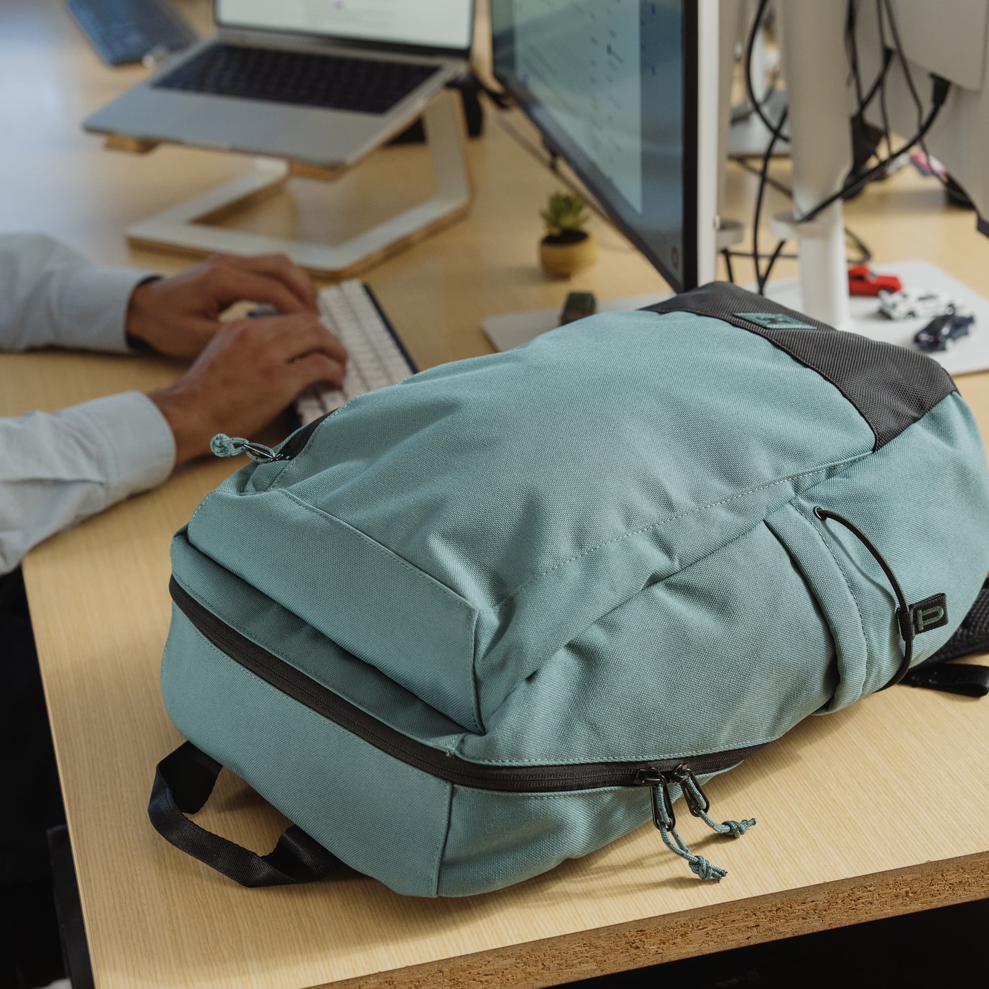 The new Recruit 22L Pack with padded laptop sleeve on a desk next to someone typing