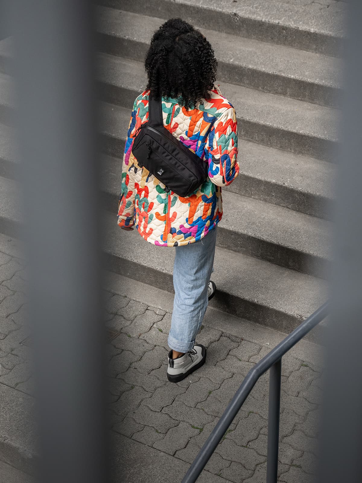 A woman walking up stairs wearing the Mini Kadet Sling in black
